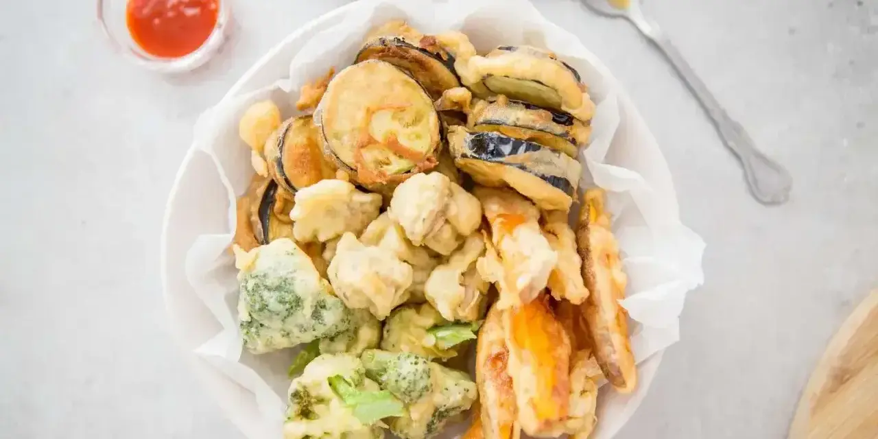 Chrupiące warzywa w cieście tempura: bakłażan, brokuły i marchewka, podane z sosem.