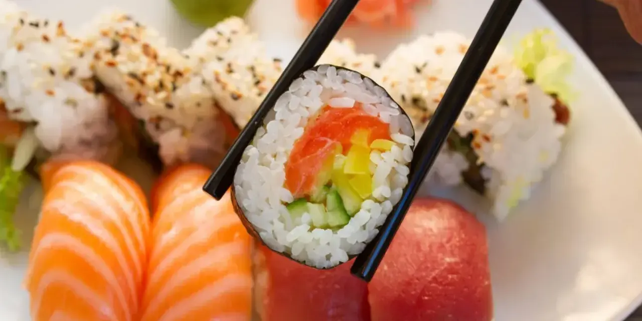 Pyszna rolka sushi z łososiem, ogórkiem i papryką, trzymana pałeczkami. Zastanawiasz się, ile waży rolka sushi?