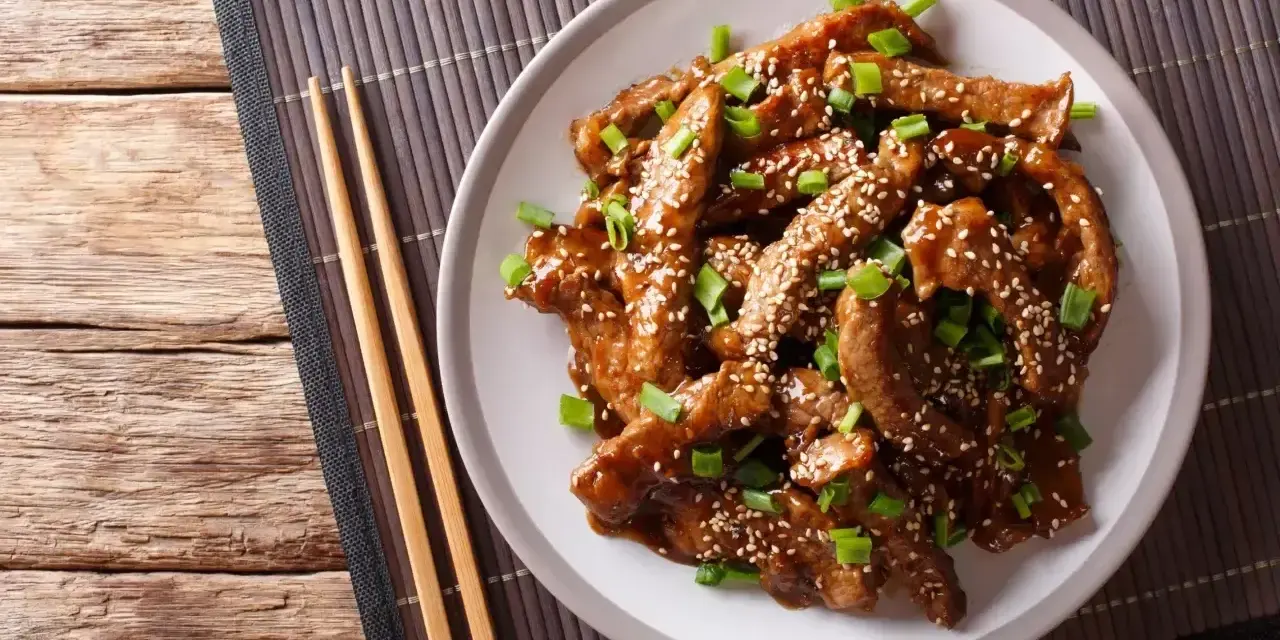 Pyszne kawałki wołowiny w sosie teriyaki, posypane sezamem i szczypiorkiem, gotowe do podania z pałeczkami.