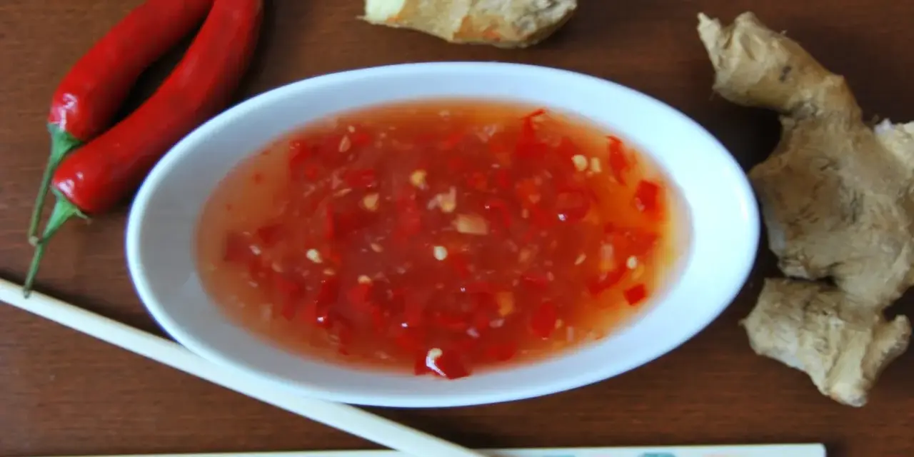Ostry sos tao tao z kawałkami chili i imbirem, obok pałeczki i papryczki.