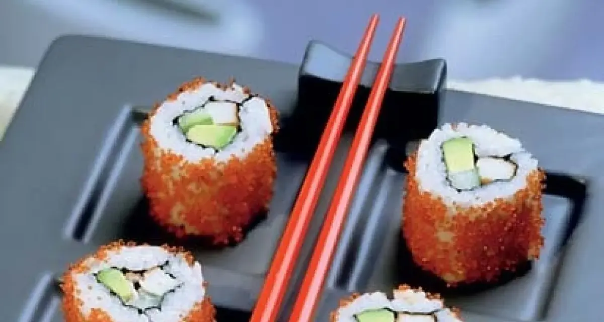 Cztery rolki sushi z awokado i rybą, obtoczone pomarańczową ikrą. Idealne sushi na diecie, podane z czerwonymi pałeczkami.