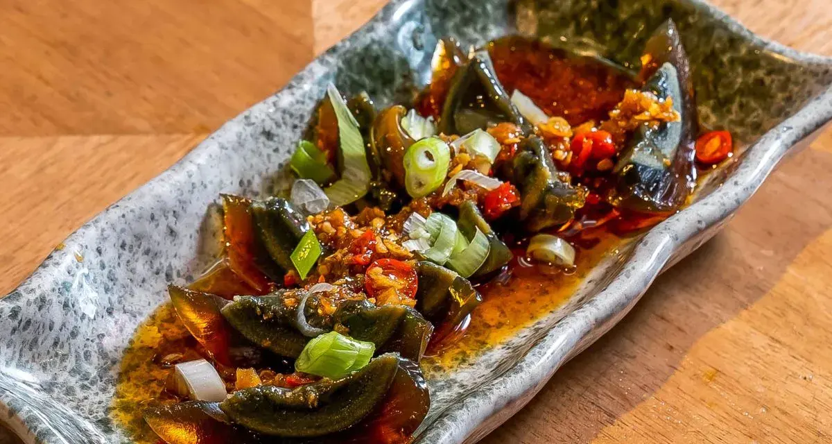 Kawałki 100 letniego jajka w pikantnym sosie z czosnkiem, chili i szczypiorkiem na kamiennej tacy.