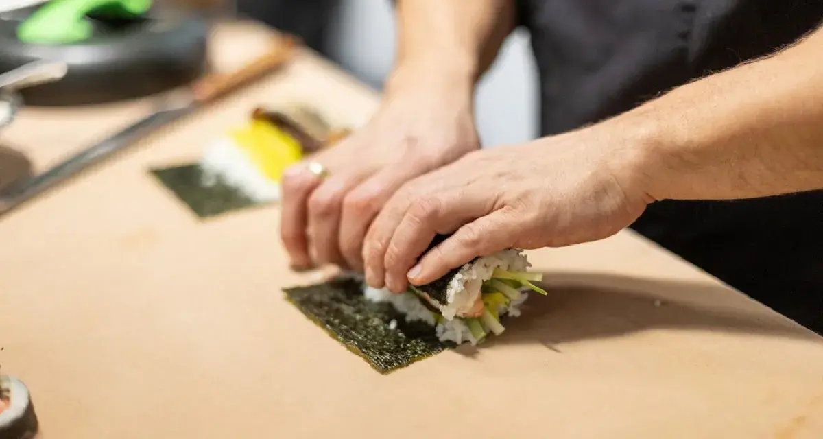 Dłonie zwijają sushi na arkuszu nori, ukazując jego wszechstronne właściwości kulinarne.