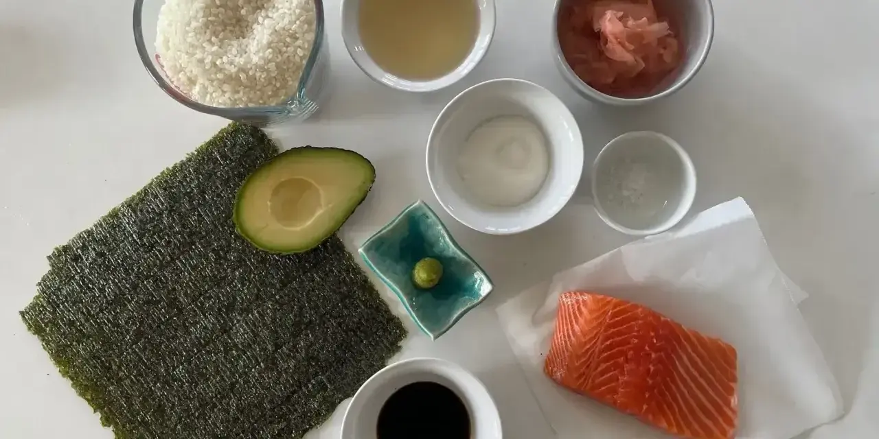 Wszystkie składniki do sushi: ryż, nori, łosoś, awokado, sos sojowy, wasabi, imbir marynowany, ocet ryżowy i sól.