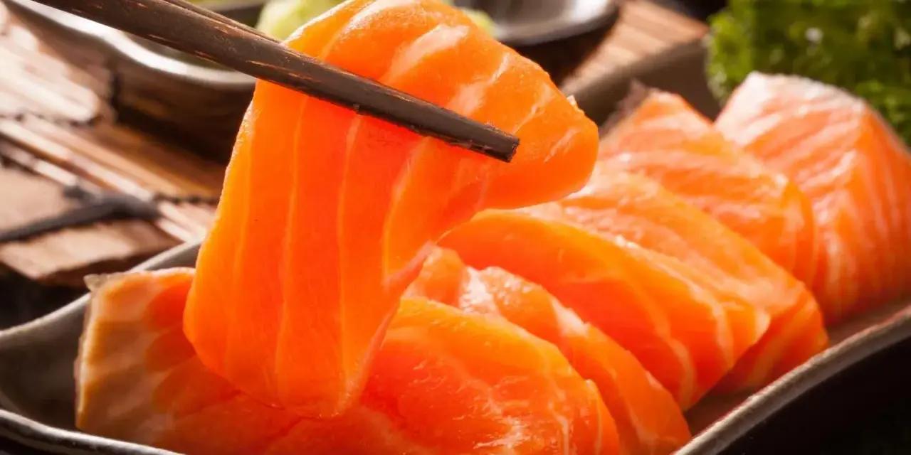 Sashimi co to? Świeży łosoś, chwytany pałeczkami, podany z wasabi i natką pietruszki.