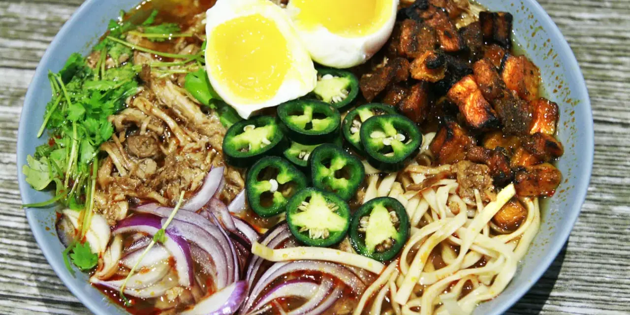 A miseczce ramen z wieprzowiną, jajkiem na pół, papryczkami jalapeño, cebulą i kolendrą.