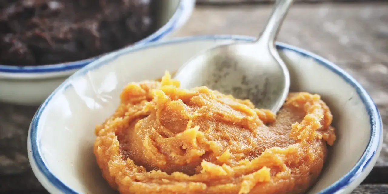 Pomarańczowa pasta miso w miseczce, obok ciemniejsza pasta. Łyżeczka zanurzona w jasnej paście.