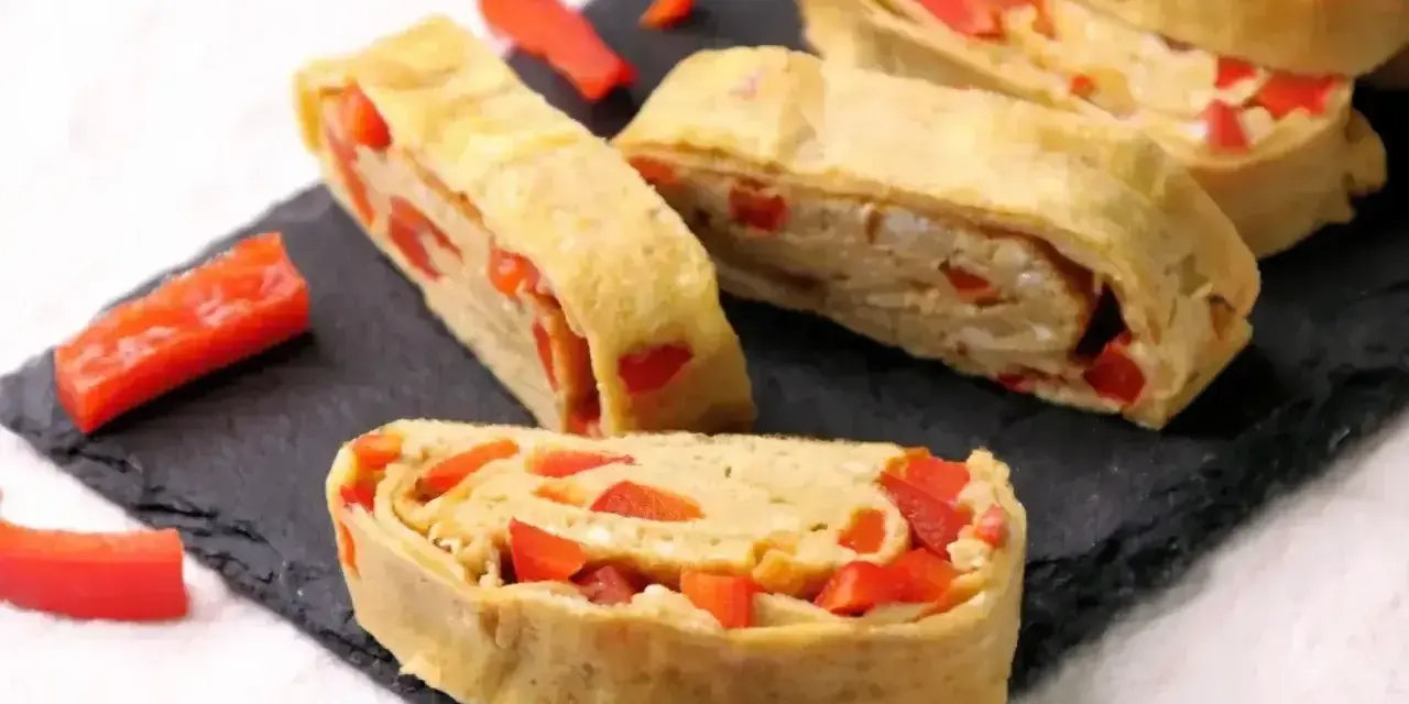 Roladki z jajek z papryką, przypominające omlet do sushi, ułożone na czarnej desce.