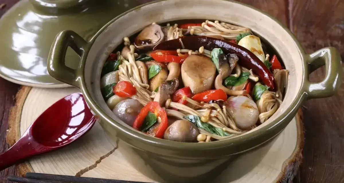 Gęsta zupa z grzybkami mun, enoki, pieczarkami, papryczkami chili i cebulką, podana w glinianym garnku.