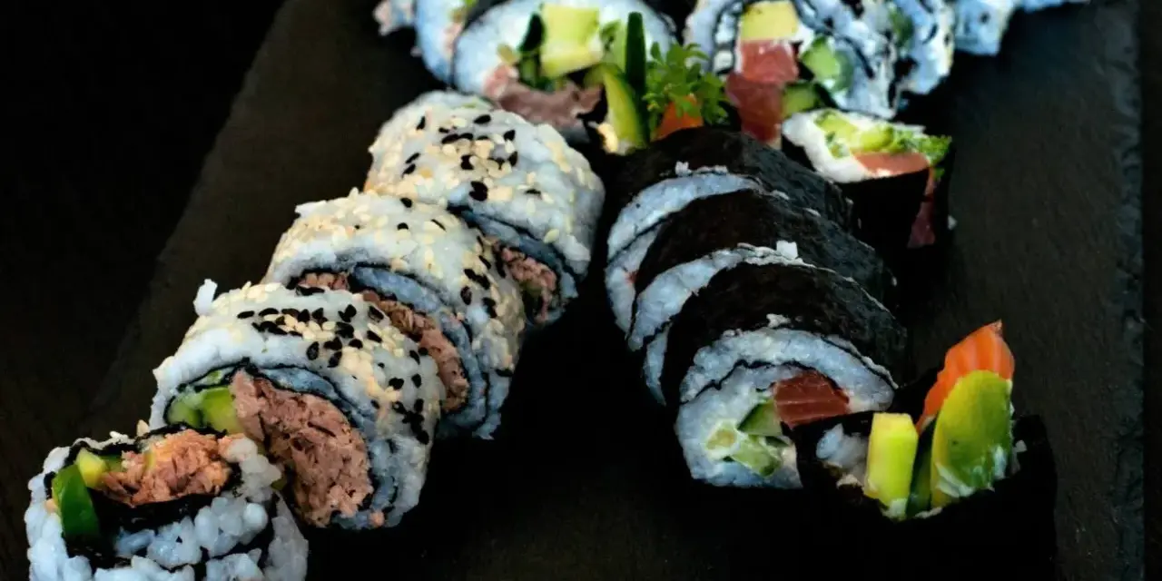Pyszne rolki sushi z tuńczykiem i awokado, posypane sezamem. Idealna rzepa do sushi na czarnej desce.