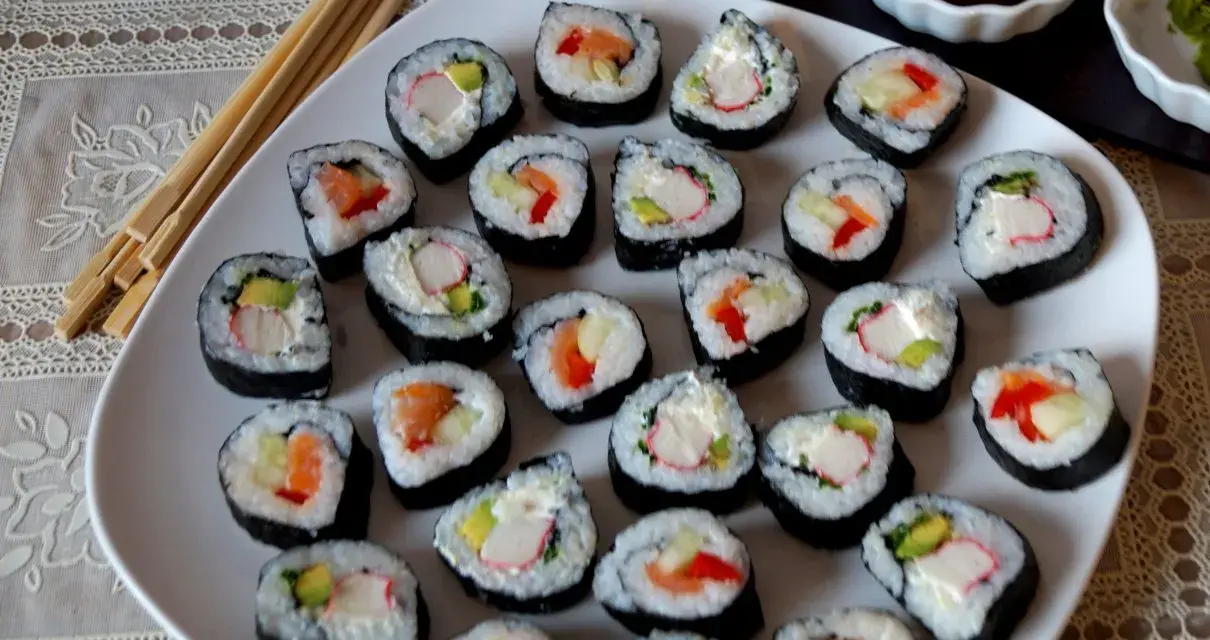 Talerz pełen sushi, w tym futomaki tamago z łososiem, awokado i paluszkami krabowymi.