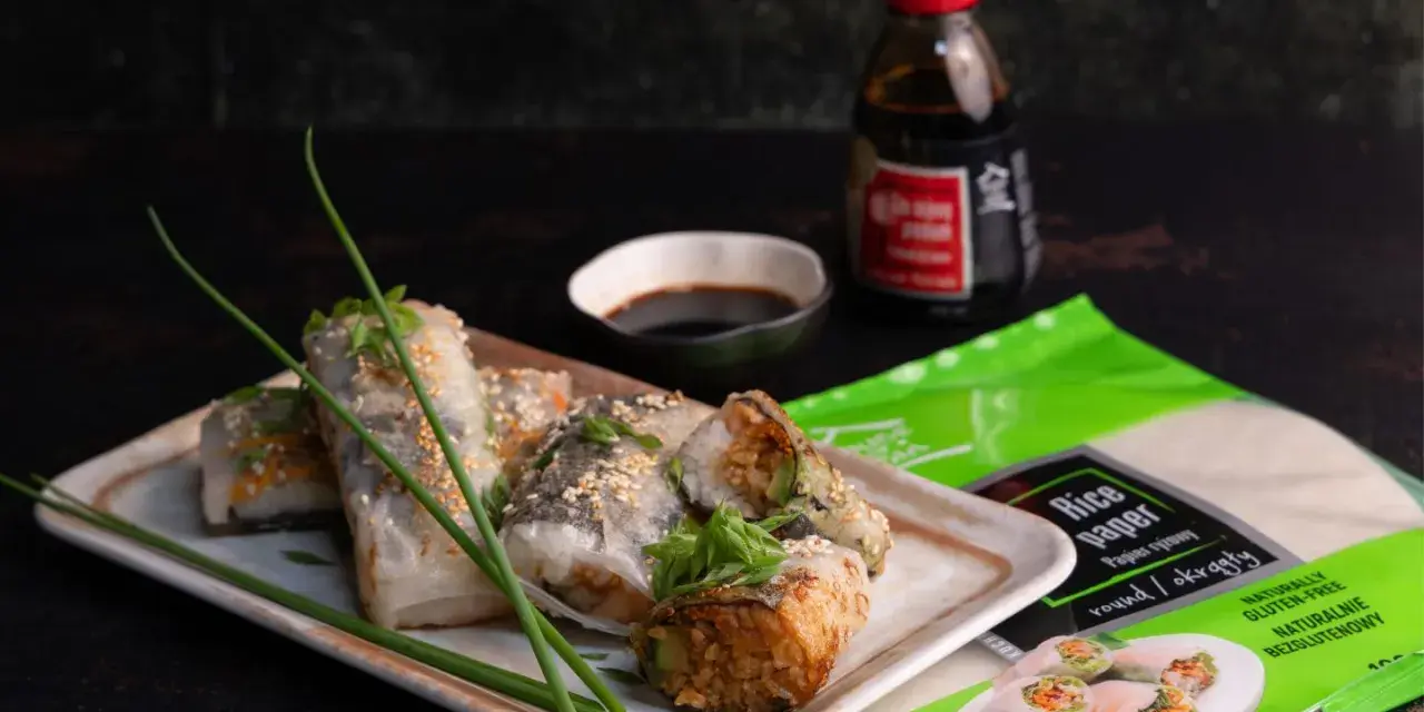 Pyszne sushi w papierze ryżowym, posypane sezamem, podane z sosem sojowym. Obok opakowanie papieru ryżowego.