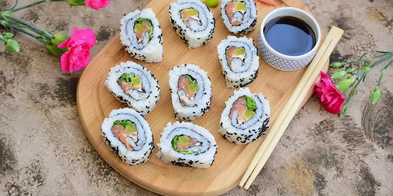 Pyszne california sushi z łososiem i awokado, posypane czarnym sezamem, podane z sosem sojowym i wasabi.