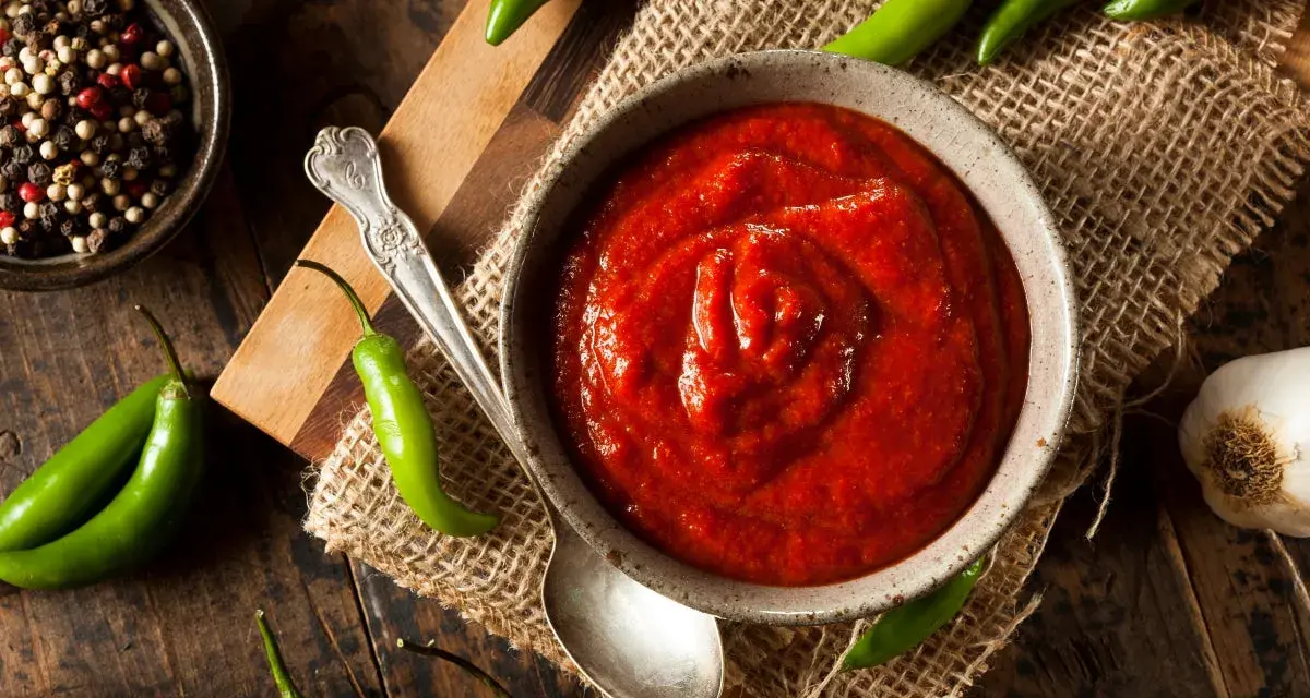 Miseczka z ostrym, czerwonym sosem, otoczona papryczkami chili, czosnkiem i pieprzem. Sriracha co to? To właśnie ten pikantny dodatek!