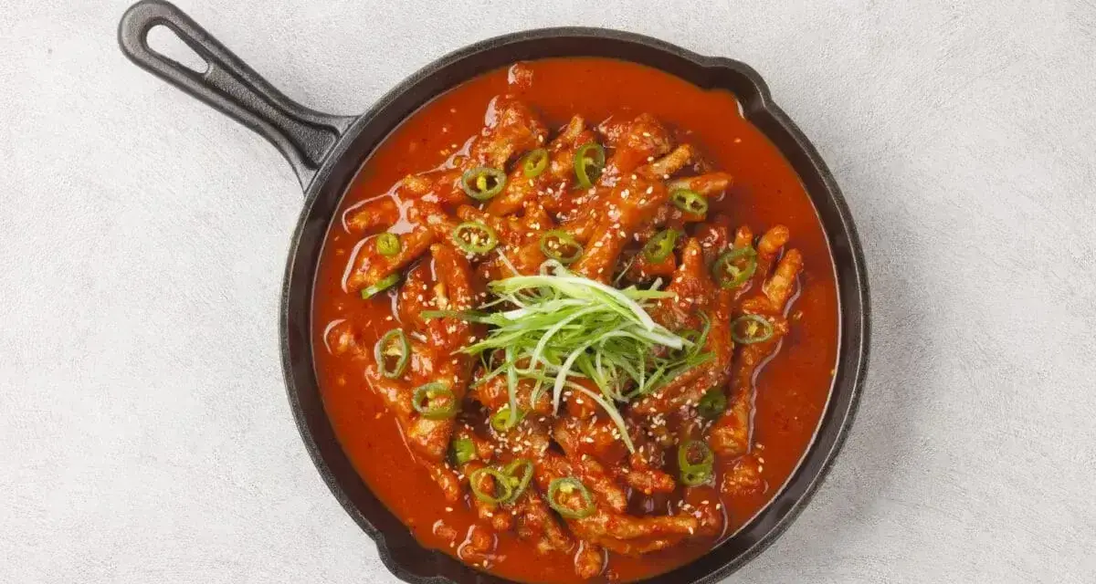 Kurczak w sosie gochujang, z zieloną cebulką i sezamem, podany na patelni.