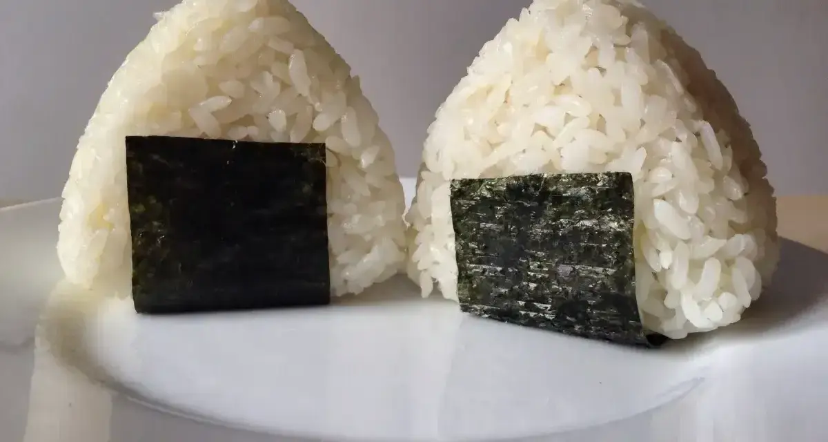 Dwa pyszne onigiri sushi, uformowane w trójkąty i ozdobione kawałkami nori, leżą na białym talerzu.