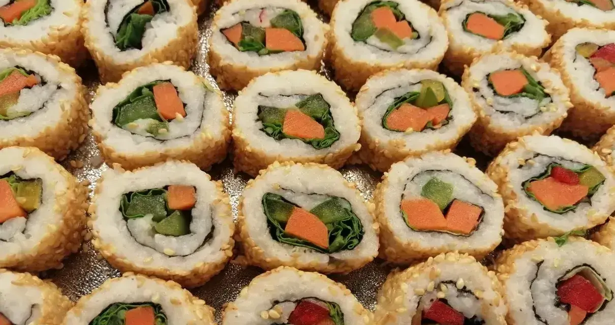 Roladki sushi z sezamem, w środku zielona sałata i pomarańczowa marchewka do sushi.
