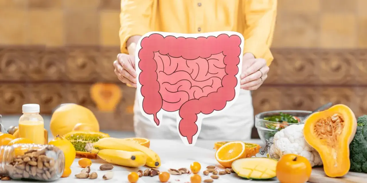Osoba trzyma planszę z jelitami, wokół owoce i orzechy. Czy sos sojowy fodmap jest bezpieczny?