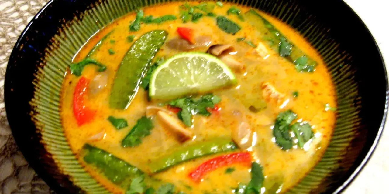 Aksamitna zupa tom kha z kurczakiem, z zielonym groszkiem, papryką i plasterkiem limonki.