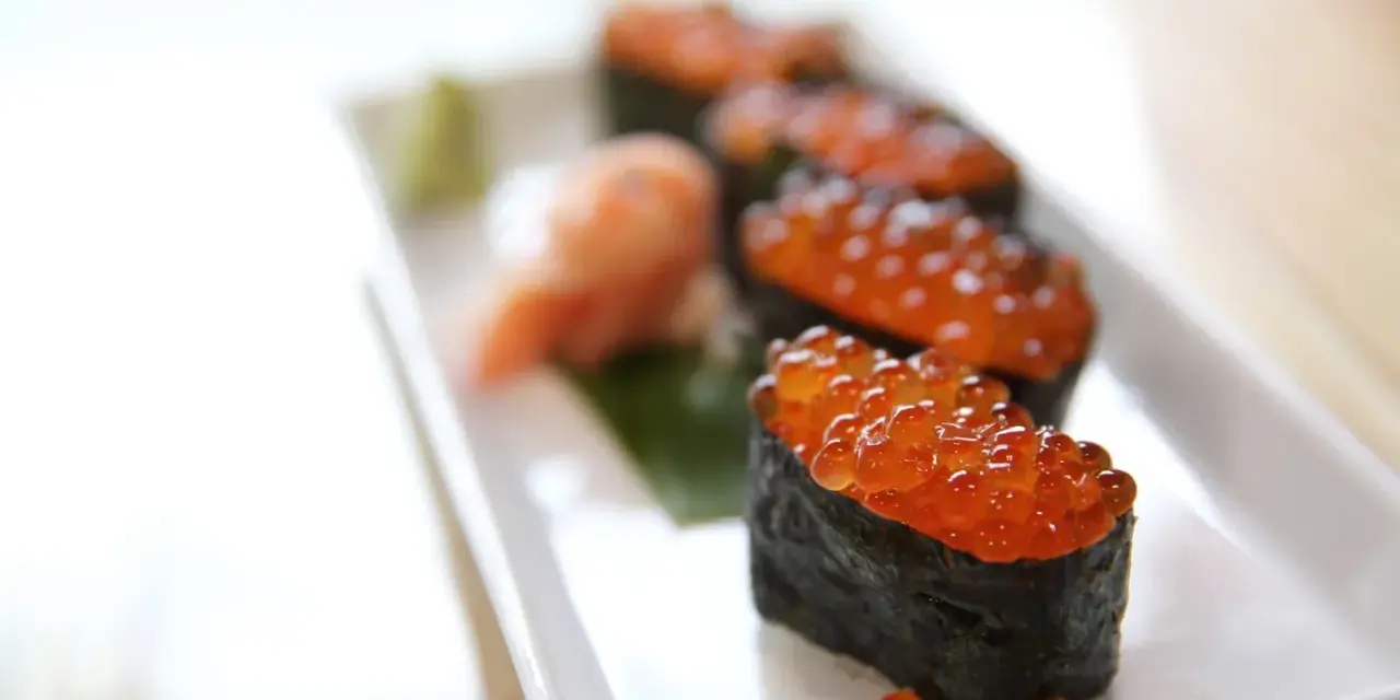 Pięć kawałków sushi z kawiorem, podanych na białym talerzu z odrobiną wasabi i marynowanego imbiru.
