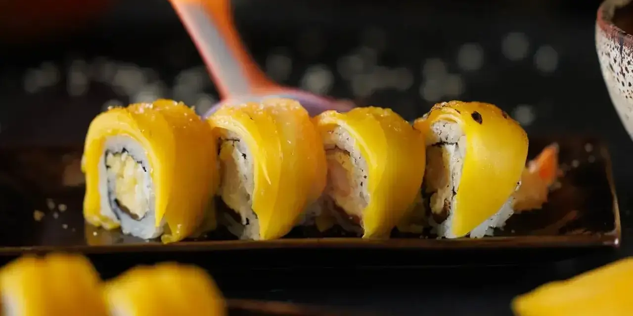 Płomień palnika opala sushi z mango, tworząc apetyczny wygląd.
