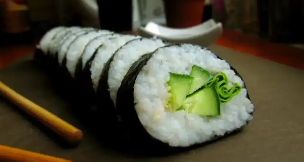 Świeży ogórek do sushi, zwinięty w rolkę z ryżem i nori. Obok leżą pałeczki.