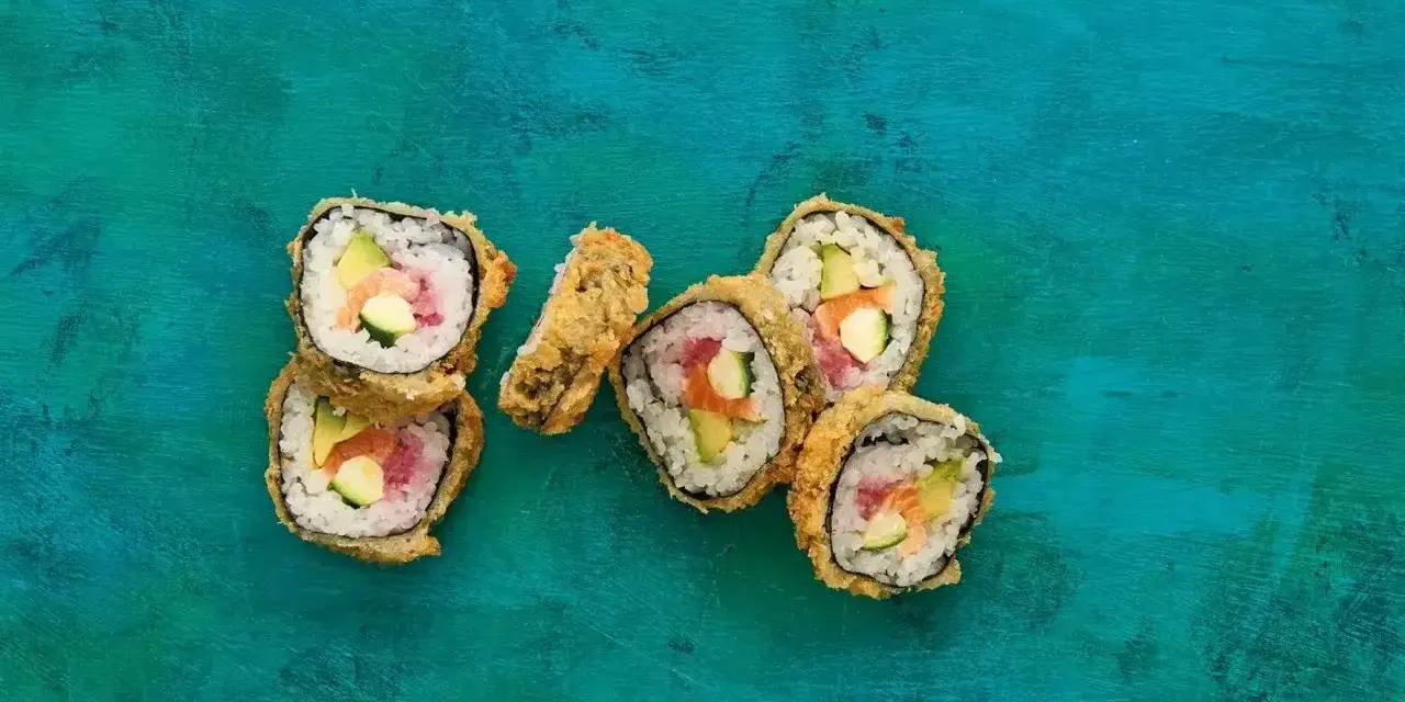 Chrupiące sushi w panierce z łososiem, awokado i ogórkiem na turkusowym tle.