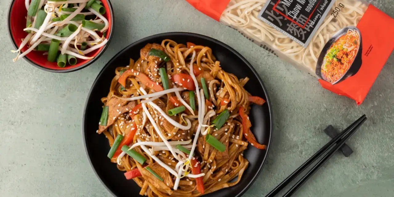 Pyszny makaron po azjatycku z kurczakiem, papryką i kiełkami fasoli mung. Obok opakowanie makaronu Chow Mein.