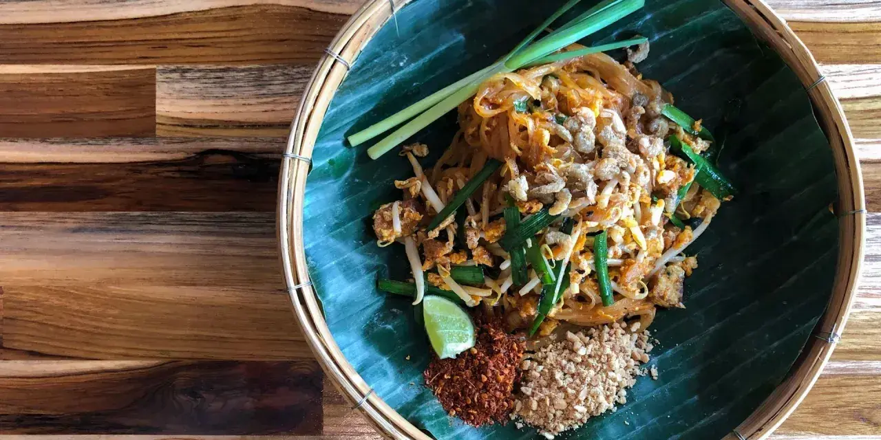 Pyszne pad thai skladniki: makaron ryżowy, kiełki, szczypiorek, orzeszki ziemne, chili i limonka na liściu bananowca.