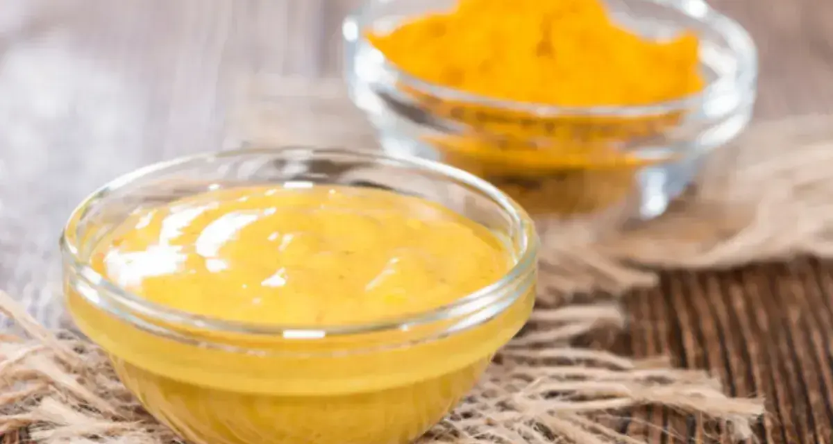 Dwie szklane miseczki na drewnianym tle. Jedna zawiera gładki sos, druga żółtą przyprawę, składniki do korma curry.