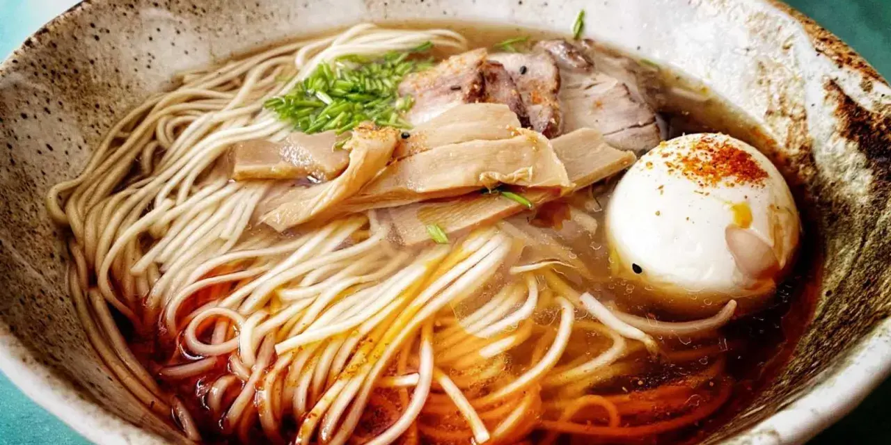 Miseczka aromatycznego ramenu z makaronem, jajkiem, mięsem i bambusem. Widać wyraźnie dodane ramen przyprawy, które nadają daniu głębi smaku.