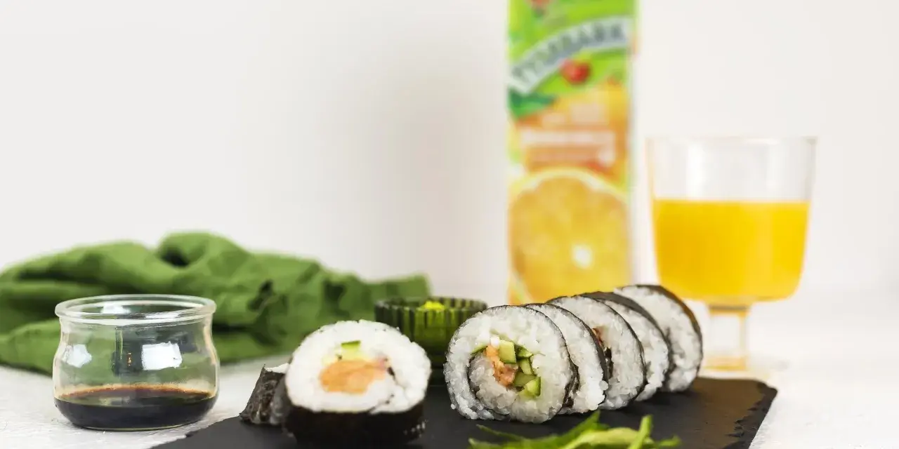 Roladki sushi z surowym łososiem do sushi, ogórkiem i ryżem, podane z sosem sojowym i sokiem pomarańczowym.