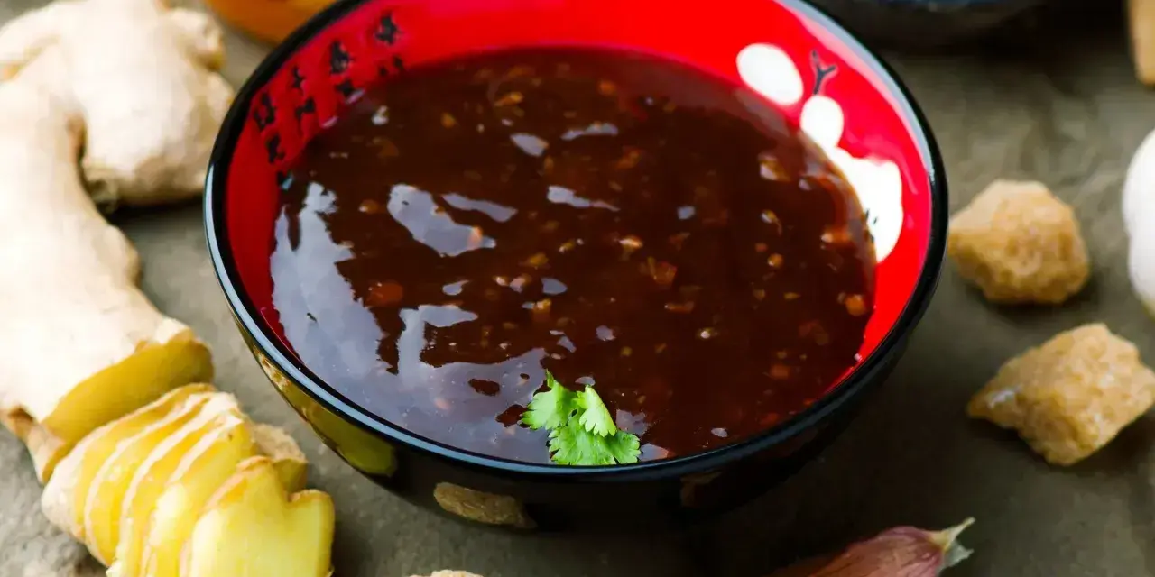 Sos teriyaki przepis: miseczka z ciemnym sosem, obok imbir, czosnek, cukier trzcinowy i miód. Idealny do dań azjatyckich.