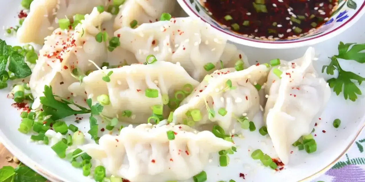 Pyszne pierożki gyoza posypane szczypiorkiem i sezamem, podane z aromatycznym sosem.