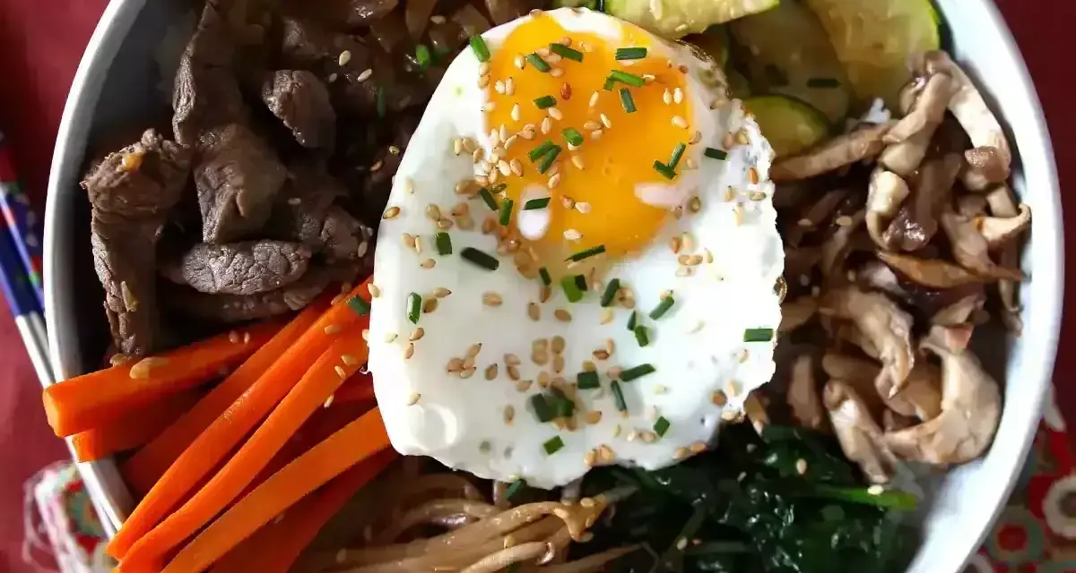 Apetyczne koreańskie dania: bibimbap z wołowiną, warzywami, grzybami i jajkiem sadzonym, posypane sezamem i szczypiorkiem.