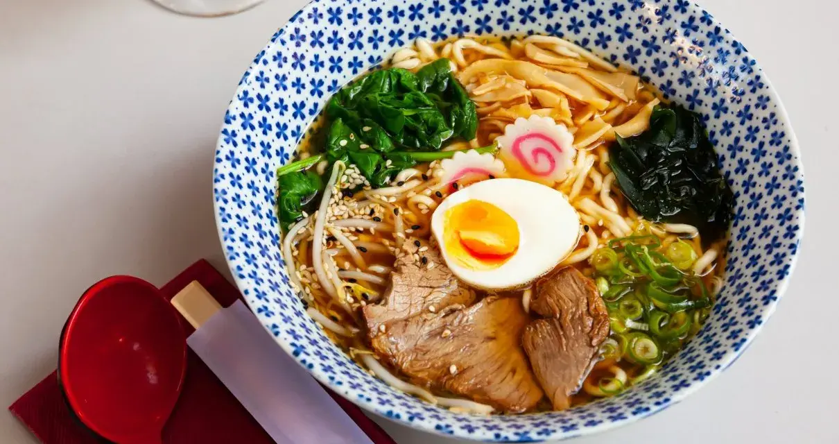 Miseczka aromatycznego makaronu ramen z jajkiem, mięsem, warzywami i kiełkami. Idealny posiłek, który dostarczy energii i zaspokoi głód.