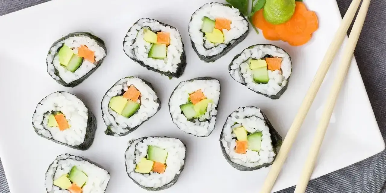 Talerz z hosomaki awokado, ogórkiem i marchewką, udekorowany wasabi i natką pietruszki.