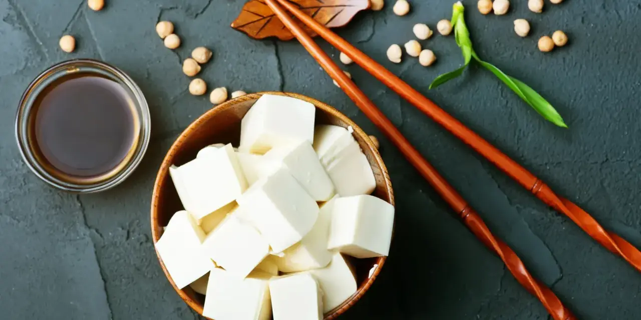 Kostki tofu, czyli przetworzona fasola sojowa, w drewnianej misce, obok sosu sojowego i pałeczek.