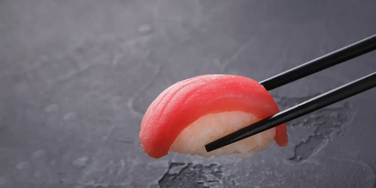 Pałeczki trzymają kawałek sushi z tuńczykiem. Czy sushi jest dobre? Wygląda apetycznie!