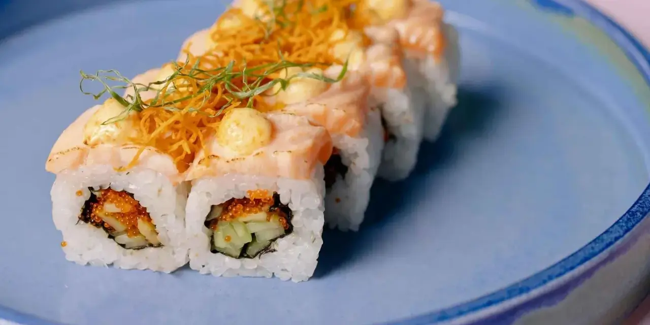 Roladki sushi z łososiem i chrupiącą posypką, z delikatnym akcentem, który przypominałby wasabi w ciąży, gdyby nie był to sos.