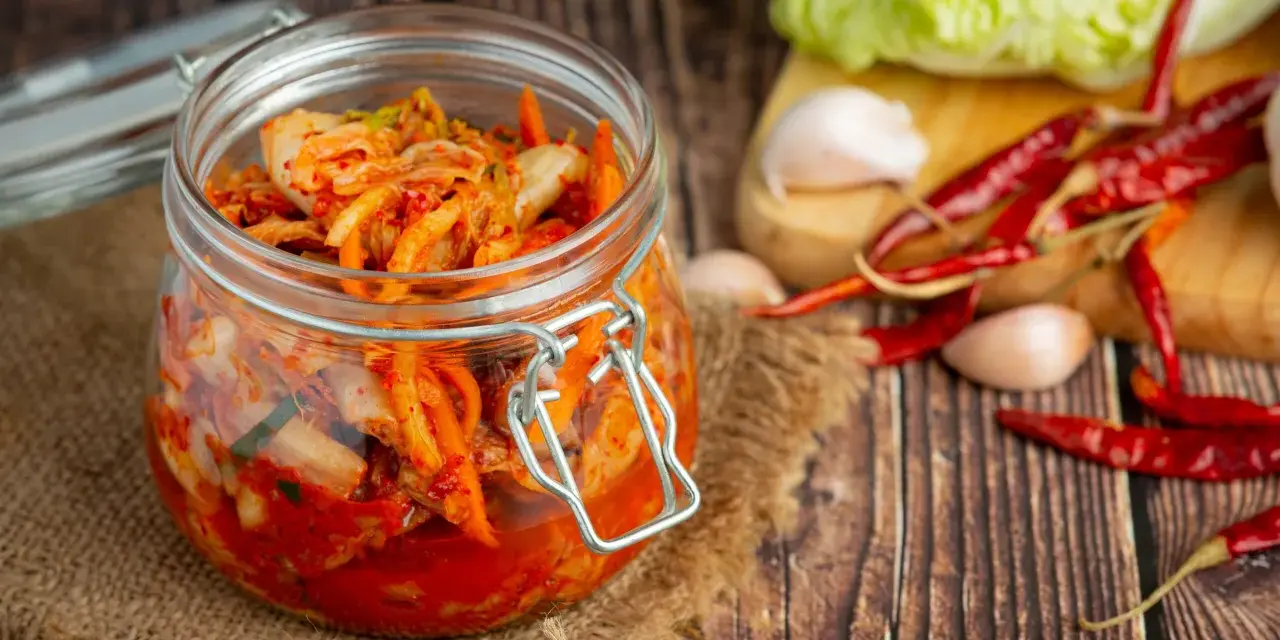 Słoik z kimchi na tle desek, z suszonymi papryczkami chili i czosnkiem.