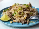 Pyszny pad thai z wołowiną, makaronem ryżowym, orzeszkami ziemnymi i ćwiartką limonki na niebieskim talerzu.