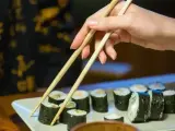 Dłoń podnosi pałeczkami rolkę sushi. Na talerzu ułożone są kawałki sushi, każdy z nich ma około 30 kcal.