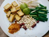 Na talerzu składniki do pad thai: smażone tofu, orzeszki ziemne, szczypiorek, kiełki fasoli mung, limonki i płatki chili. Gotowy sos pad thai czeka!