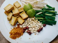 Na talerzu składniki do pad thai: smażone tofu, orzeszki ziemne, szczypiorek, kiełki fasoli mung, limonki i płatki chili. Gotowy sos pad thai czeka!