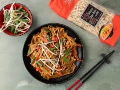 Pyszny makaron po azjatycku z kurczakiem, papryką i kiełkami fasoli mung. Obok opakowanie makaronu Chow Mein.