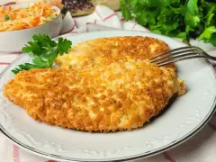 Dwa chrupiące kotlety z kurczaka w panko, podane na talerzu z sałatką z kapusty i marchewki.