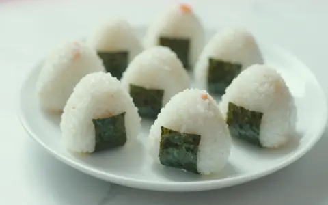 Kilka pysznych onigiri z łososiem, udekorowanych kawałkami nori, ułożonych na białym talerzu.