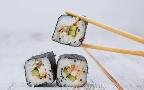 Rolka sushi z ogórkiem i rybą, podniesiona pałeczkami. Zastanawiasz się, ile octu ryżowego na 500g ryżu?