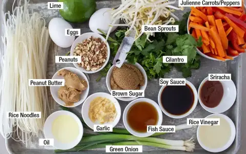 Składniki do sosu pad thai: makaron ryżowy, jajka, orzeszki ziemne, masło orzechowe, olej, czosnek, zielona cebulka, brązowy cukier, kiełki fasoli, kolendra, marchewka, papryka, sos sojowy, sos rybny, ocet ryżowy, sriracha, limonka.